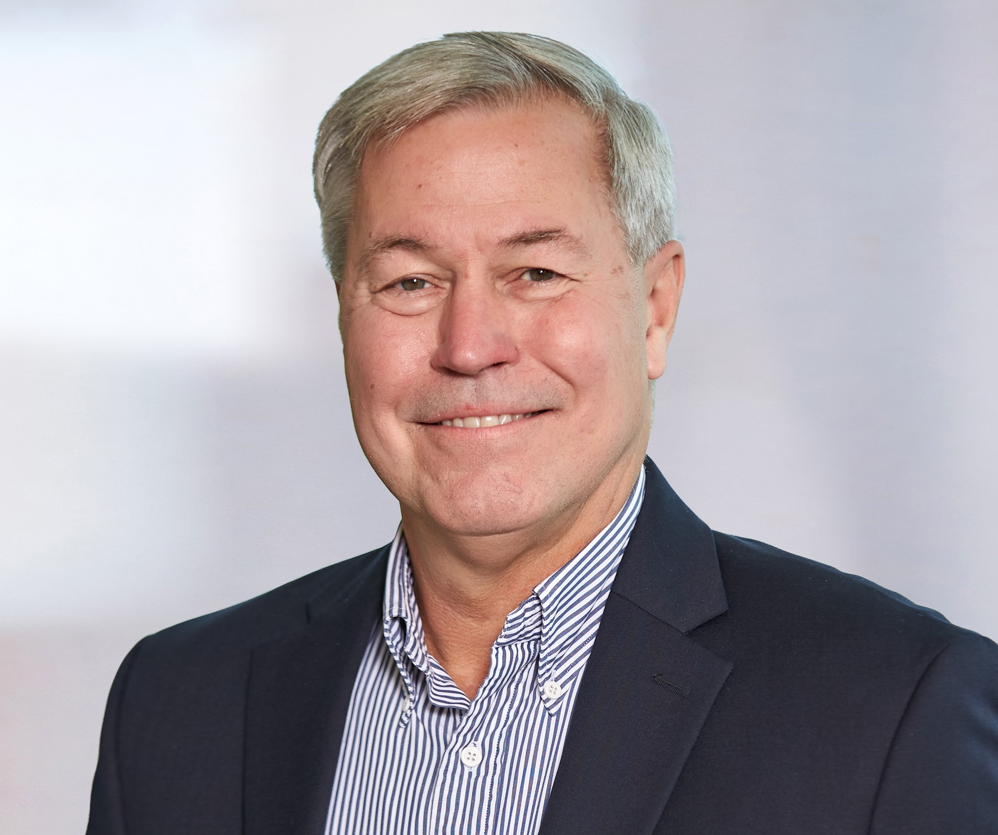 A headshot of Larry Fabrety with short grey hair parted to the side wearing a blazer and a striped button up shirt.